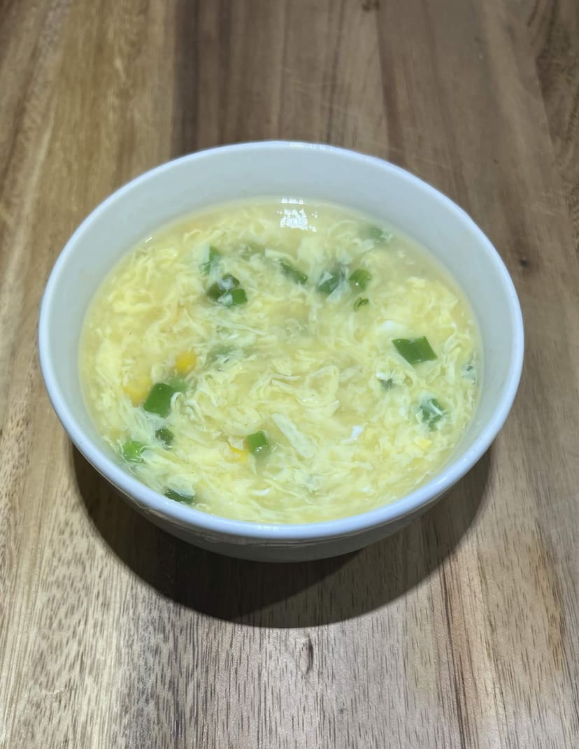 Golden egg drop soup in a bowl with delicate egg ribbons and sliced scallions on top.