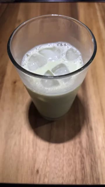 A tall glass filled with milk, ice, and vibrant green whisked matcha layered on top.