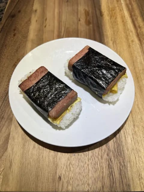 A rectangle of turkey spam and fried egg over seasoned sushi rice wrapped tightly in a strip of dark nori seaweed.
